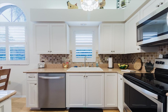 kitchen featuring stainless steel appliances, a sink, plenty of natural light, and white cabinets