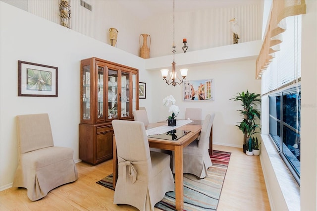 dining area with a high ceiling, a chandelier, light wood finished floors, and baseboards
