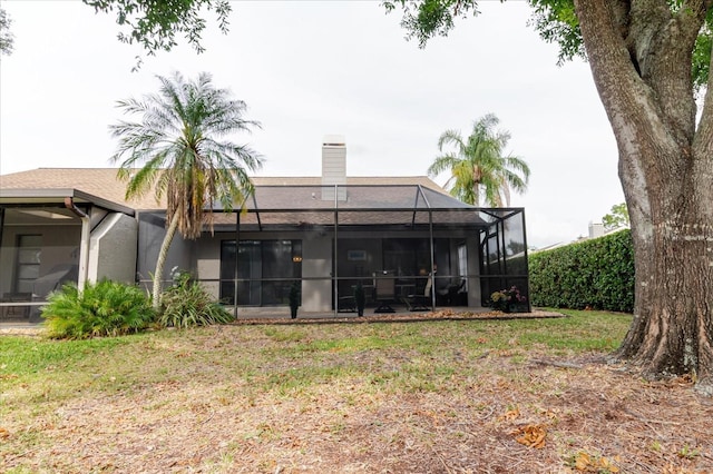 rear view of house with a yard, a chimney, and a lanai