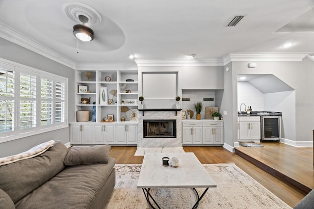 9722 Tiffany Oaks Ln, Tampa, FL 33612 - living area with wine cooler, a premium fireplace, crown molding, a ceiling fan, and light wood-type flooring