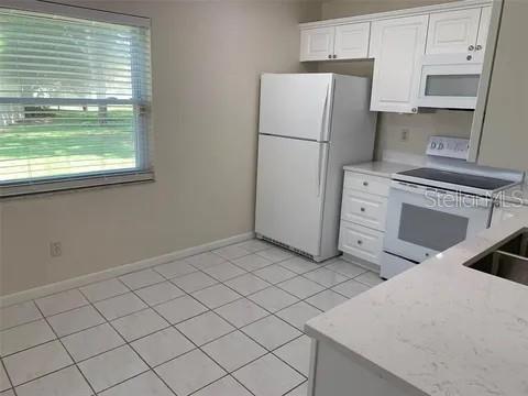 2720 Sand Hollow Ct Unit 156A, Clearwater, FL 33761 - kitchen featuring white appliances, white cabinetry, baseboards, light tile patterned floors, and light stone countertops