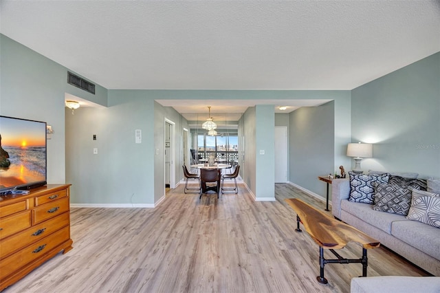 31 Island Way Unit 1403, Clearwater Beach, FL 33767 - living room featuring light wood-style flooring, baseboards, a textured ceiling, and a chandelier