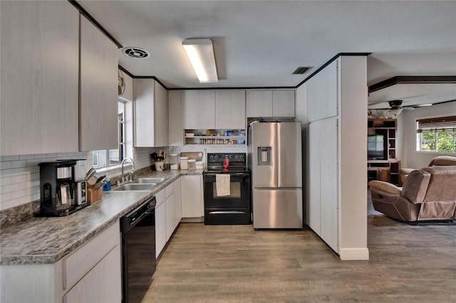 kitchen featuring black appliances, a sink, open floor plan, light wood-style flooring, and backsplash