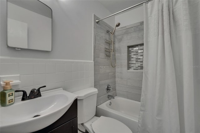full bathroom with shower / tub combo, toilet, vanity, a wainscoted wall, and tile walls