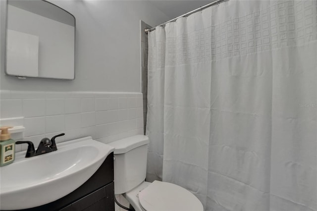 bathroom featuring toilet, tile walls, vanity, wainscoting, and a shower with curtain