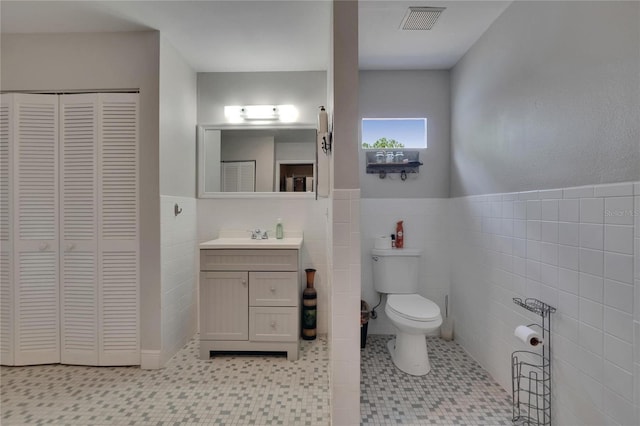 bathroom featuring toilet, tile walls, a closet, vanity, and a wainscoted wall