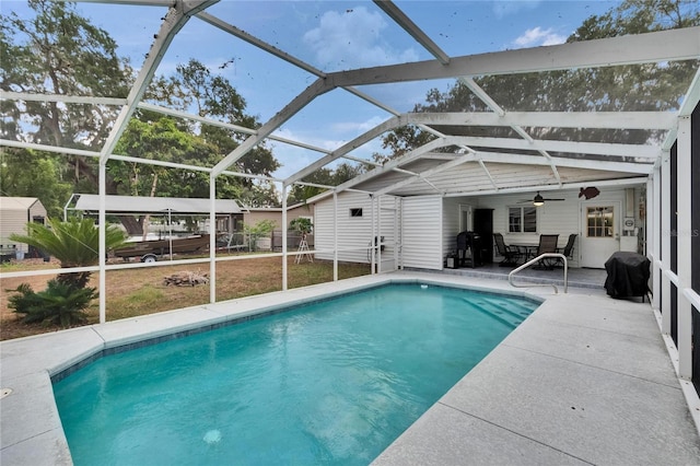 swimming pool with a patio, ceiling fan, a lanai, and an outbuilding