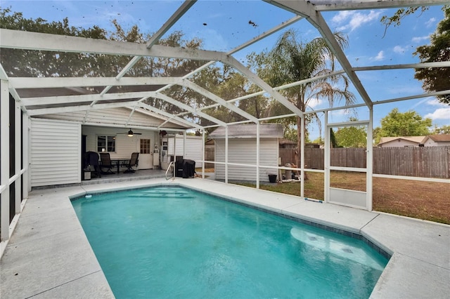 view of pool featuring a shed, an outbuilding, a patio, ceiling fan, and glass enclosure