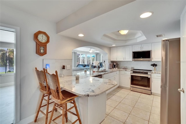 6530 Manila Palm Way, Apollo Beach, FL 33572 - kitchen with stainless steel appliances, a peninsula, decorative backsplash, white cabinets, and a sink