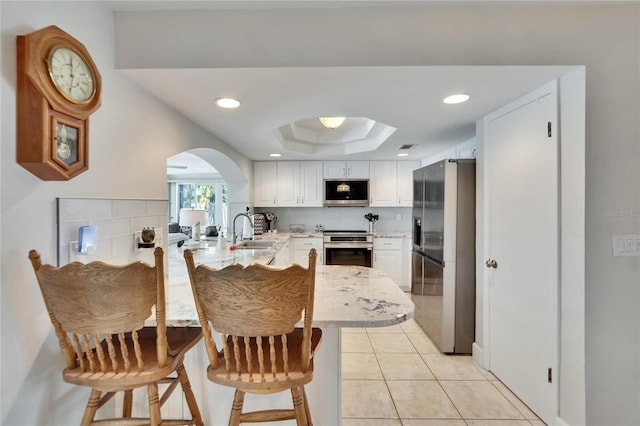 6530 Manila Palm Way, Apollo Beach, FL 33572 - kitchen featuring appliances with stainless steel finishes, a peninsula, arched walkways, white cabinetry, and a raised ceiling
