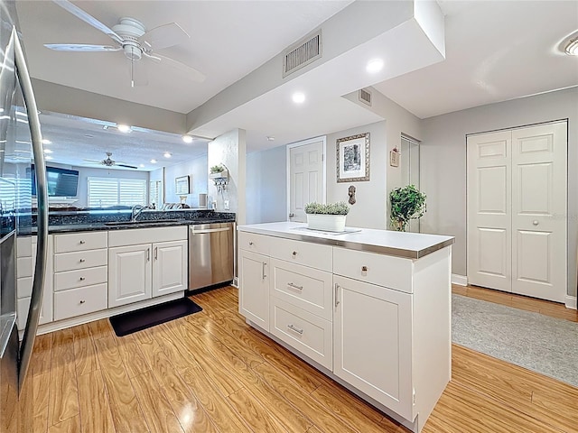 120 1st St E Unit 104, Saint Petersburg, FL 33715 - kitchen with stainless steel dishwasher, ceiling fan, open floor plan, light wood-type flooring, and white cabinets