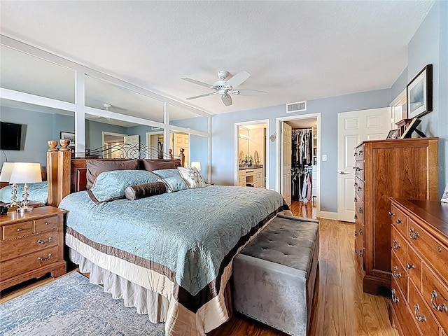 120 1st St E Unit 104, Saint Petersburg, FL 33715 - bedroom with light wood-style floors, a spacious closet, a closet, a ceiling fan, and ensuite bathroom