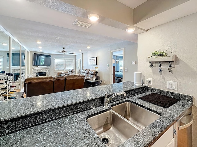 120 1st St E Unit 104, Saint Petersburg, FL 33715 - kitchen featuring a textured wall, a fireplace, ceiling fan, dark stone counters, and dishwasher