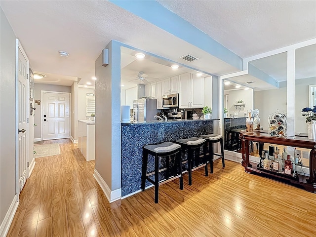 120 1st St E Unit 104, Saint Petersburg, FL 33715 - kitchen featuring stainless steel appliances, light wood-style floors, ceiling fan, a kitchen breakfast bar, and a textured ceiling