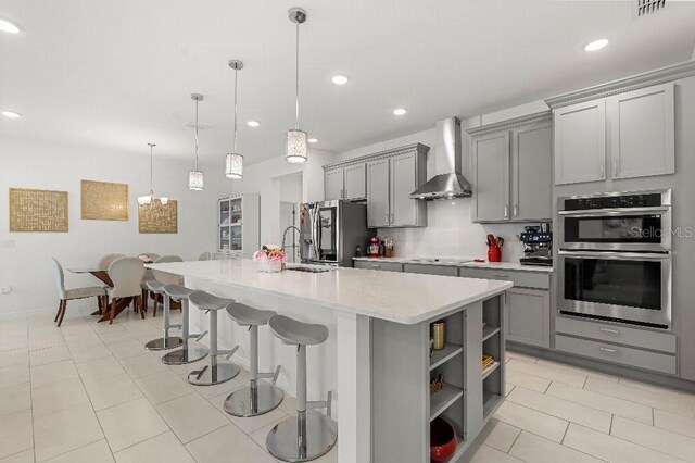 921 Fieldstone Way, Haines City, FL 33844 - kitchen with gray cabinets, wall chimney range hood, appliances with stainless steel finishes, a sink, and a kitchen island with sink