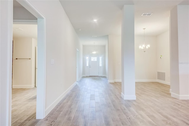 corridor featuring light wood-style flooring, a chandelier, and baseboards