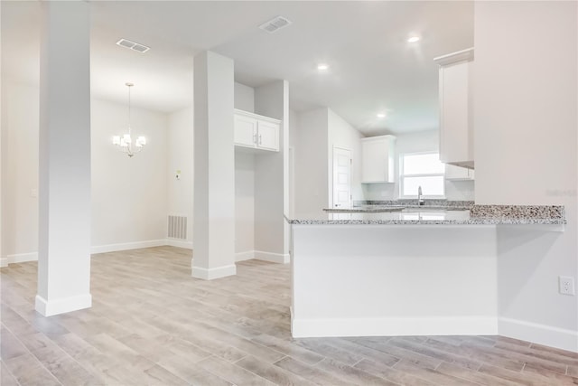 kitchen with light wood finished floors, a peninsula, white cabinets, light stone countertops, and recessed lighting