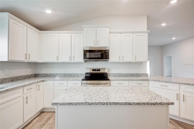 kitchen with appliances with stainless steel finishes, lofted ceiling, white cabinetry, light wood-style floors, and a center island