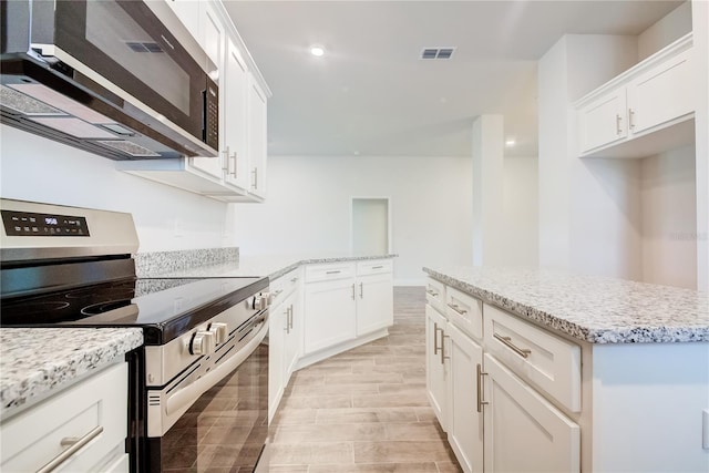 kitchen with appliances with stainless steel finishes, white cabinetry, light stone counters, and light wood-style floors