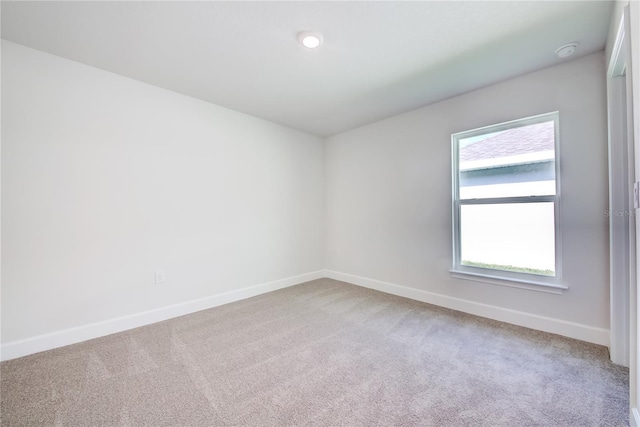empty room featuring light carpet, baseboards, and a smoke detector
