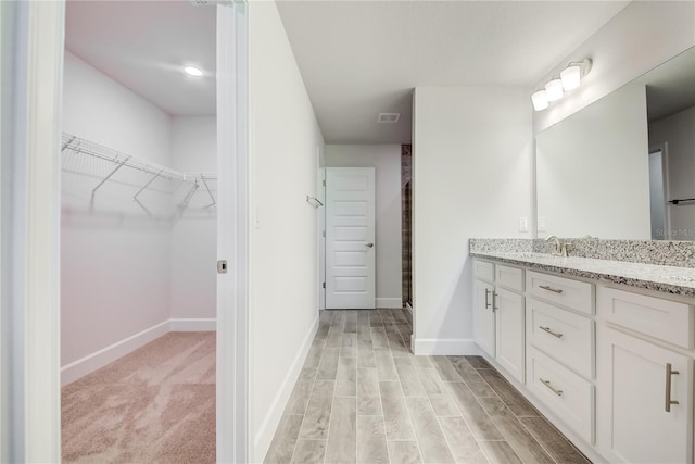 bathroom with vanity, baseboards, a spacious closet, a shower stall, and wood finished floors