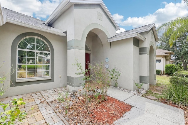 view of exterior entry featuring stucco siding and roof with shingles