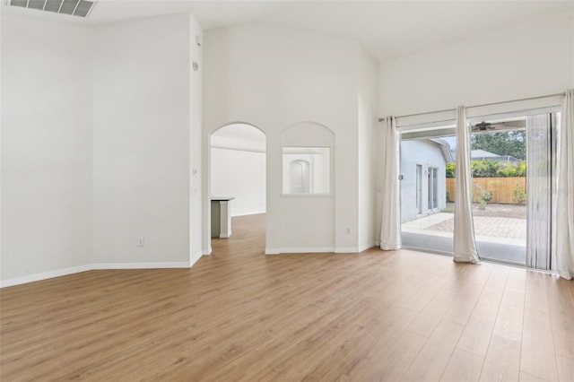 unfurnished living room featuring light wood-style floors, baseboards, arched walkways, and lofted ceiling
