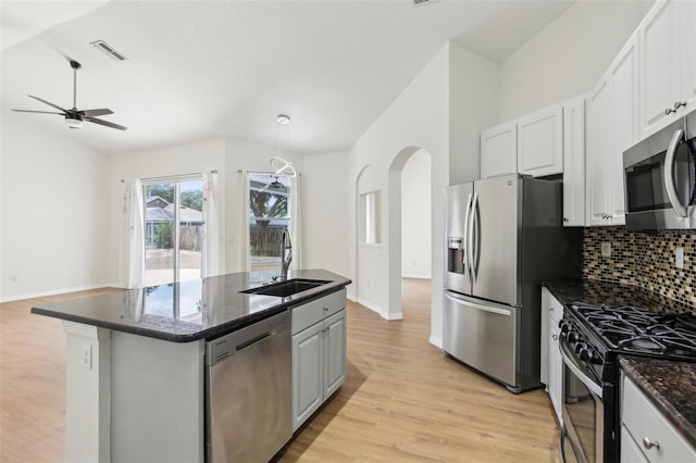 kitchen featuring appliances with stainless steel finishes, a sink, light wood finished floors, ceiling fan, and decorative backsplash