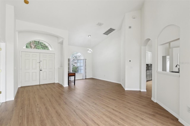 foyer entrance featuring arched walkways, light wood-style flooring, high vaulted ceiling, and baseboards
