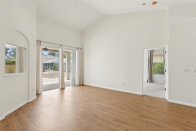 empty room featuring high vaulted ceiling, light wood-style floors, and baseboards