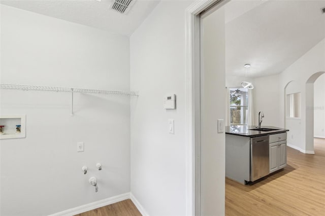 laundry room with a sink, light wood finished floors, baseboards, and hookup for a gas dryer