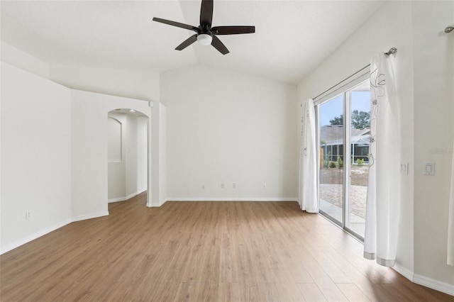 spare room featuring light wood-type flooring, arched walkways, ceiling fan, baseboards, and vaulted ceiling