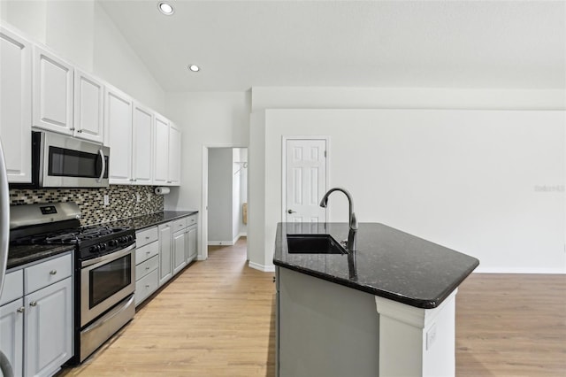 kitchen featuring stainless steel appliances, a sink, backsplash, a kitchen island with sink, and light wood-style flooring
