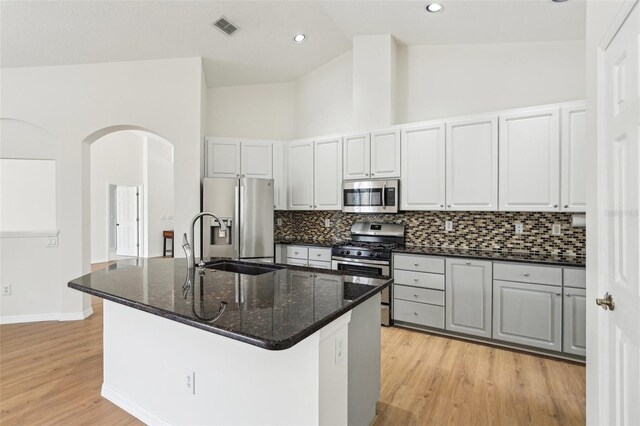 kitchen with appliances with stainless steel finishes, arched walkways, light wood finished floors, backsplash, and high vaulted ceiling