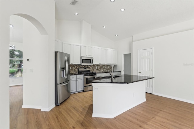 kitchen featuring appliances with stainless steel finishes, dark countertops, light wood finished floors, white cabinetry, and high vaulted ceiling