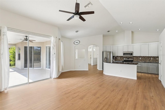 kitchen featuring stainless steel appliances, open floor plan, a ceiling fan, dark countertops, and vaulted ceiling