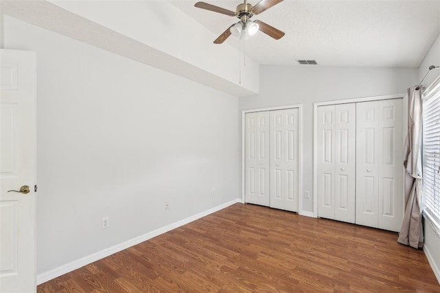 unfurnished bedroom with vaulted ceiling, wood finished floors, multiple closets, and multiple windows