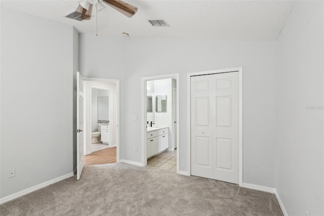 unfurnished bedroom featuring light colored carpet, lofted ceiling, ensuite bathroom, a closet, and baseboards
