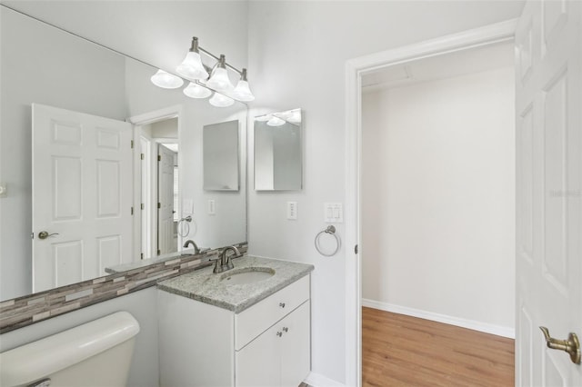 half bath featuring wood finished floors, toilet, vanity, and baseboards