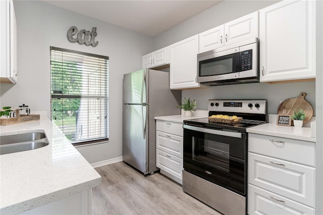 kitchen featuring appliances with stainless steel finishes, white cabinets, light wood-type flooring, baseboards, and a sink