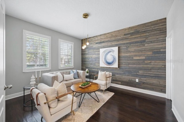 living room with an accent wall, baseboards, wood walls, and dark wood-style flooring