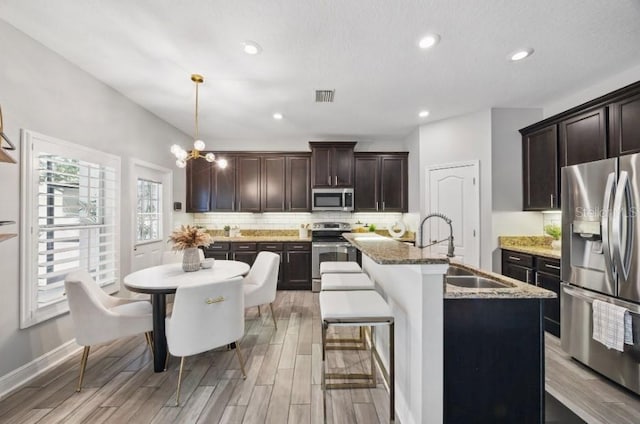 kitchen with appliances with stainless steel finishes, a sink, backsplash, light wood finished floors, and recessed lighting
