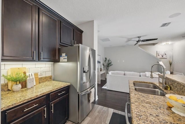 kitchen featuring a sink, stainless steel refrigerator with ice dispenser, open floor plan, light wood-style flooring, and decorative backsplash