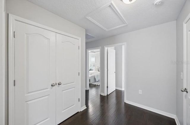 unfurnished bedroom featuring attic access, baseboards, a closet, dark wood-style flooring, and a textured ceiling