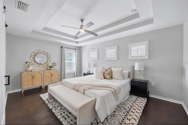 bedroom featuring a tray ceiling, baseboards, wood finished floors, and ceiling fan
