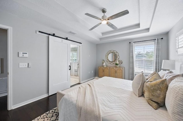 bedroom with a barn door, baseboards, wood finished floors, and a raised ceiling