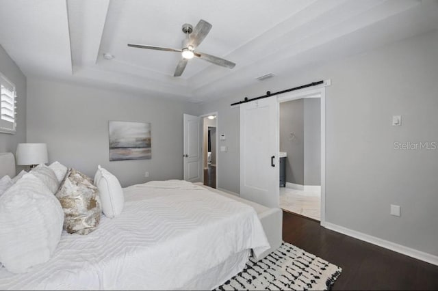 bedroom featuring a barn door, a raised ceiling, dark wood-style flooring, baseboards, and ceiling fan