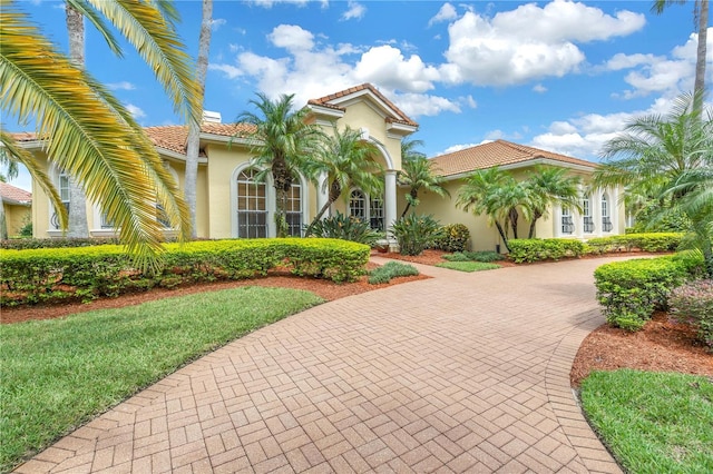 mediterranean / spanish home featuring stucco siding, curved driveway, a tiled roof, and a front yard