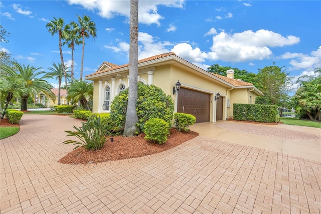 view of home's exterior with decorative driveway, an attached garage, stucco siding, and a chimney
