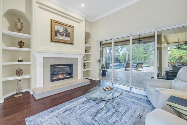 living area featuring built in shelves, wood finished floors, crown molding, baseboards, and ceiling fan